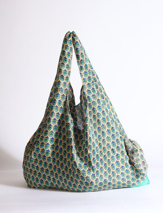Blue reusable bag with tropical floral pattern in pink, yellow, and green, shown hanging with handles visible