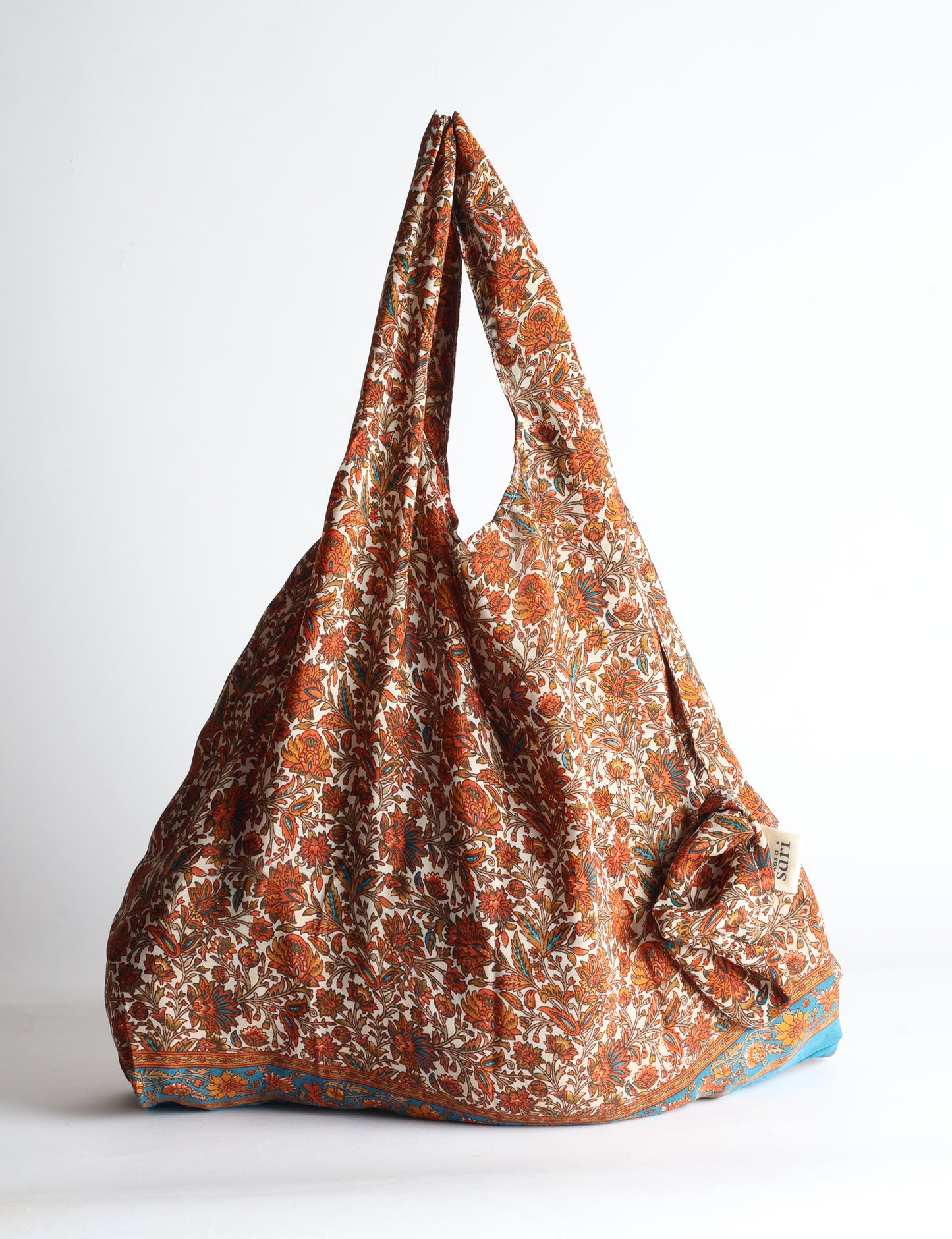 Blue reusable bag with tropical floral pattern in pink, yellow, and green, shown hanging with handles visible