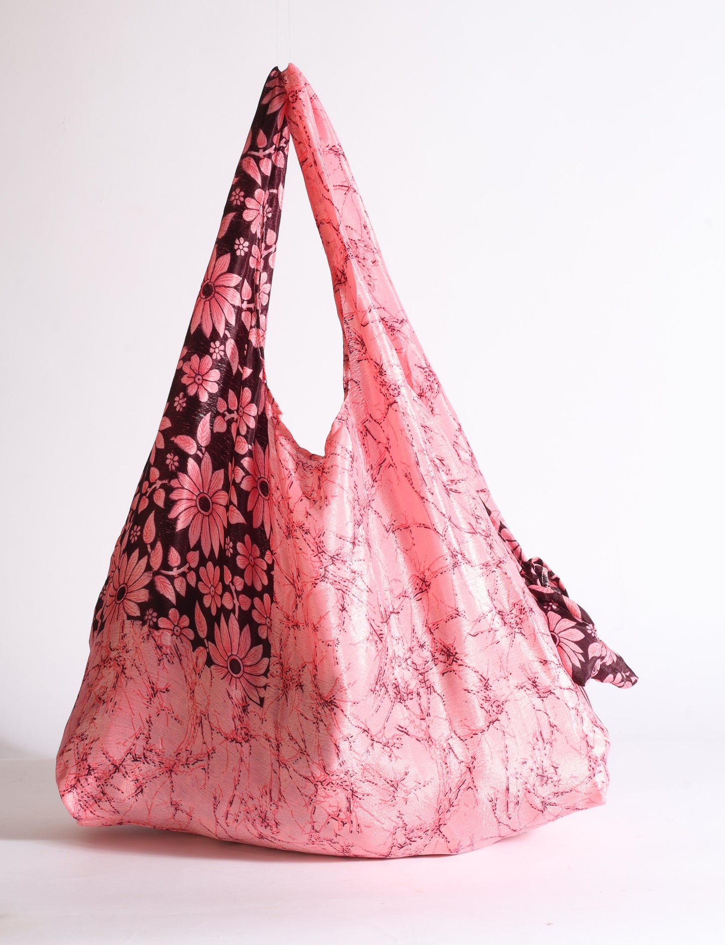 Blue reusable bag with tropical floral pattern in pink, yellow, and green, shown hanging with handles visible