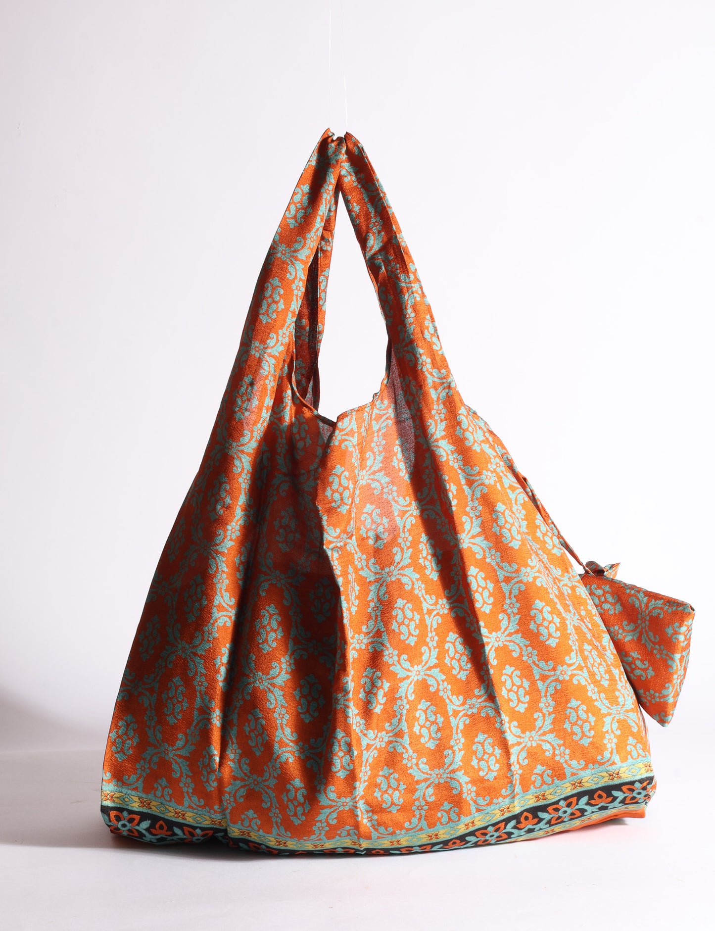Blue reusable bag with tropical floral pattern in pink, yellow, and green, shown hanging with handles visible