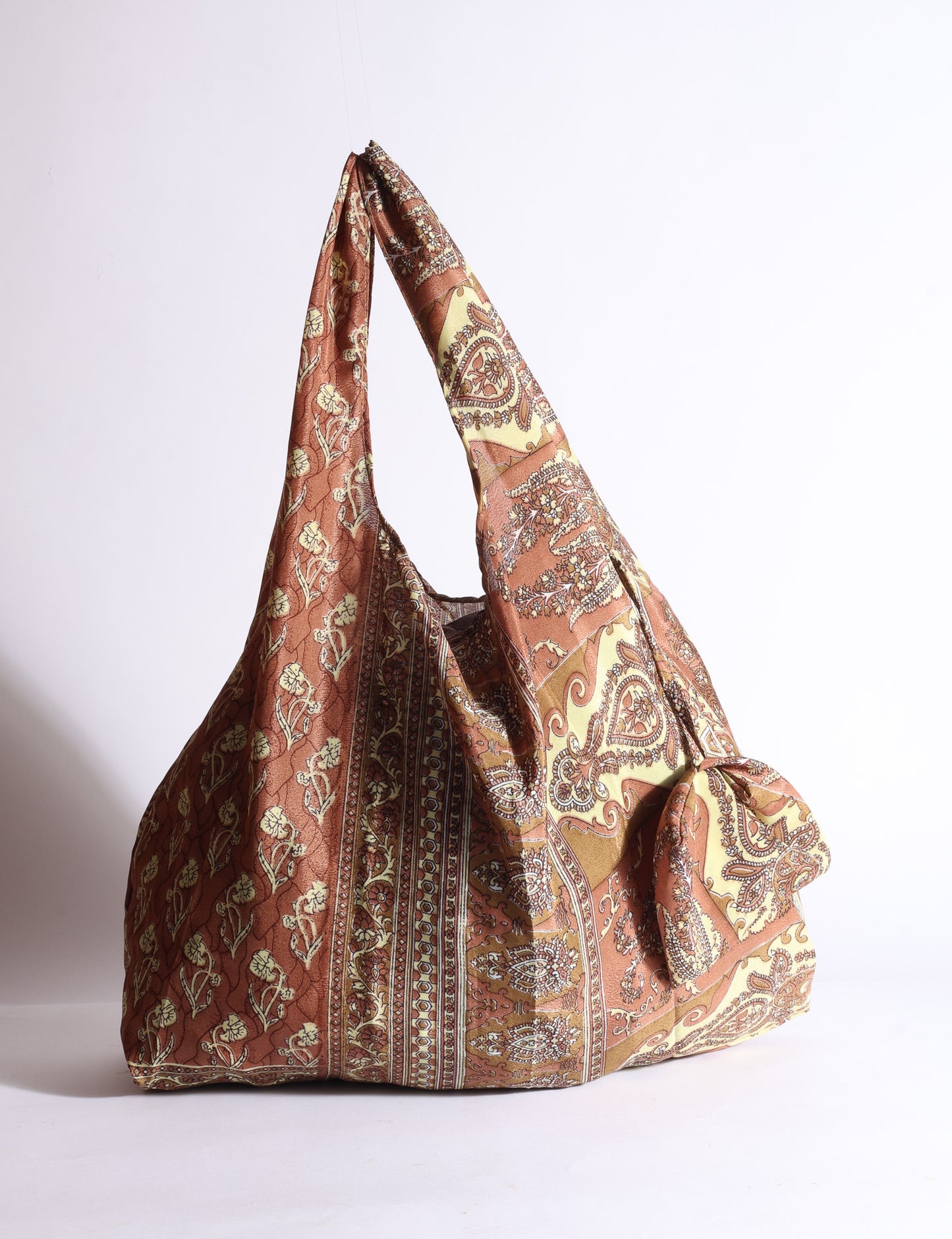 Blue reusable bag with tropical floral pattern in pink, yellow, and green, shown hanging with handles visible