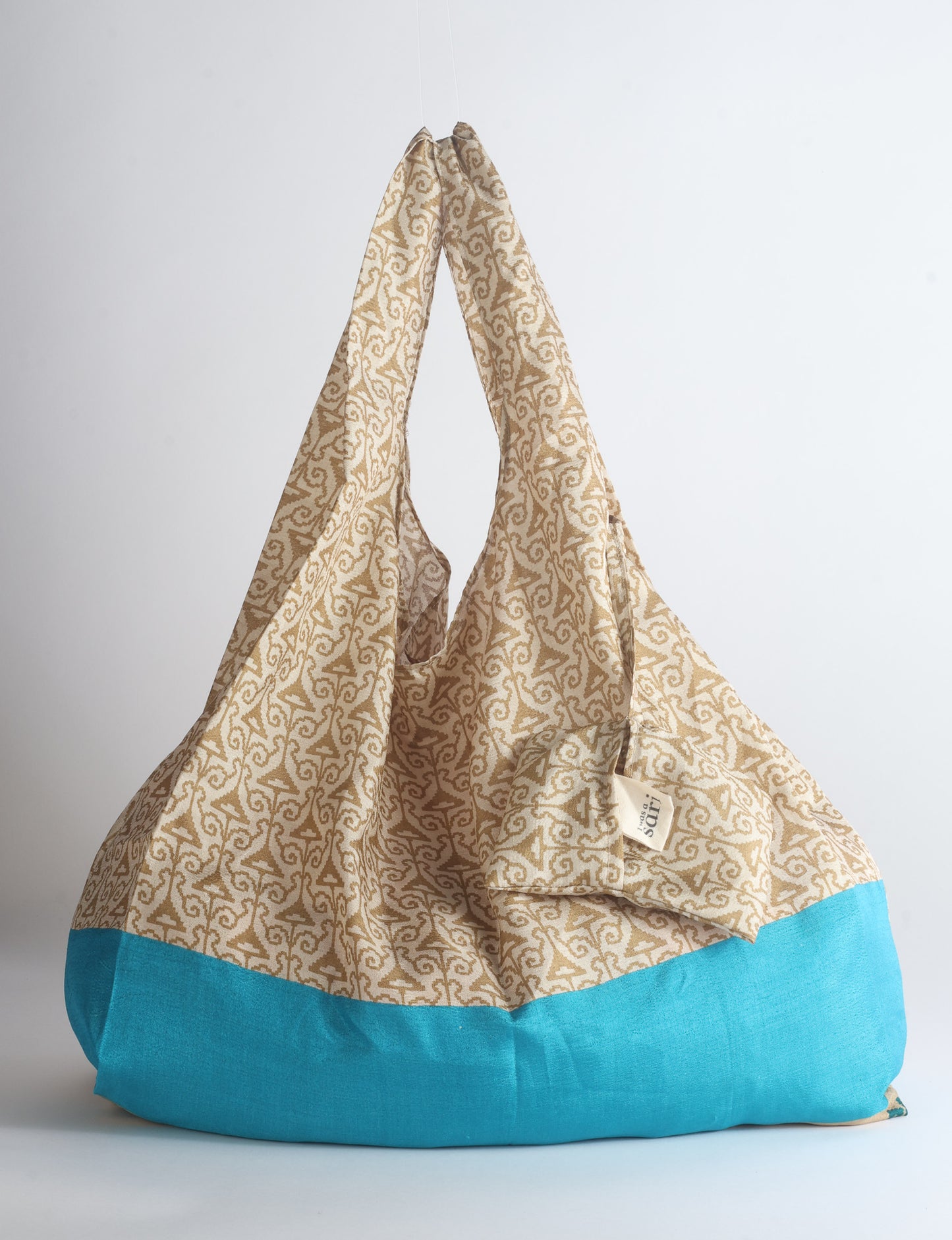 Blue reusable bag with tropical floral pattern in pink, yellow, and green, shown hanging with handles visible