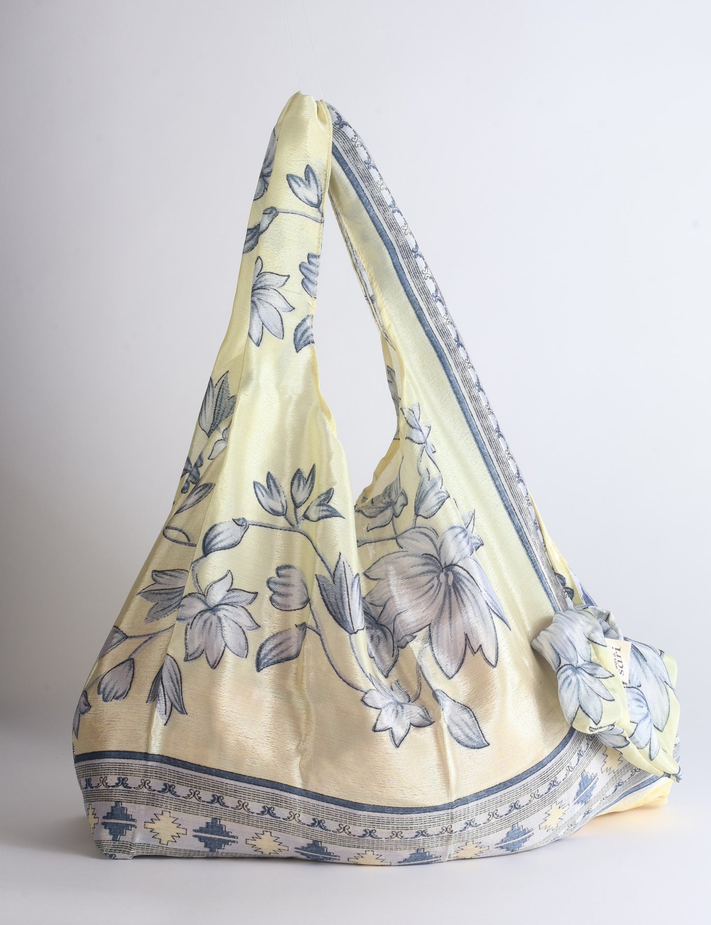 Blue reusable bag with tropical floral pattern in pink, yellow, and green, shown hanging with handles visible