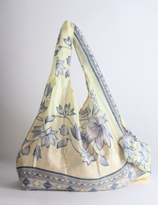 Blue reusable bag with tropical floral pattern in pink, yellow, and green, shown hanging with handles visible