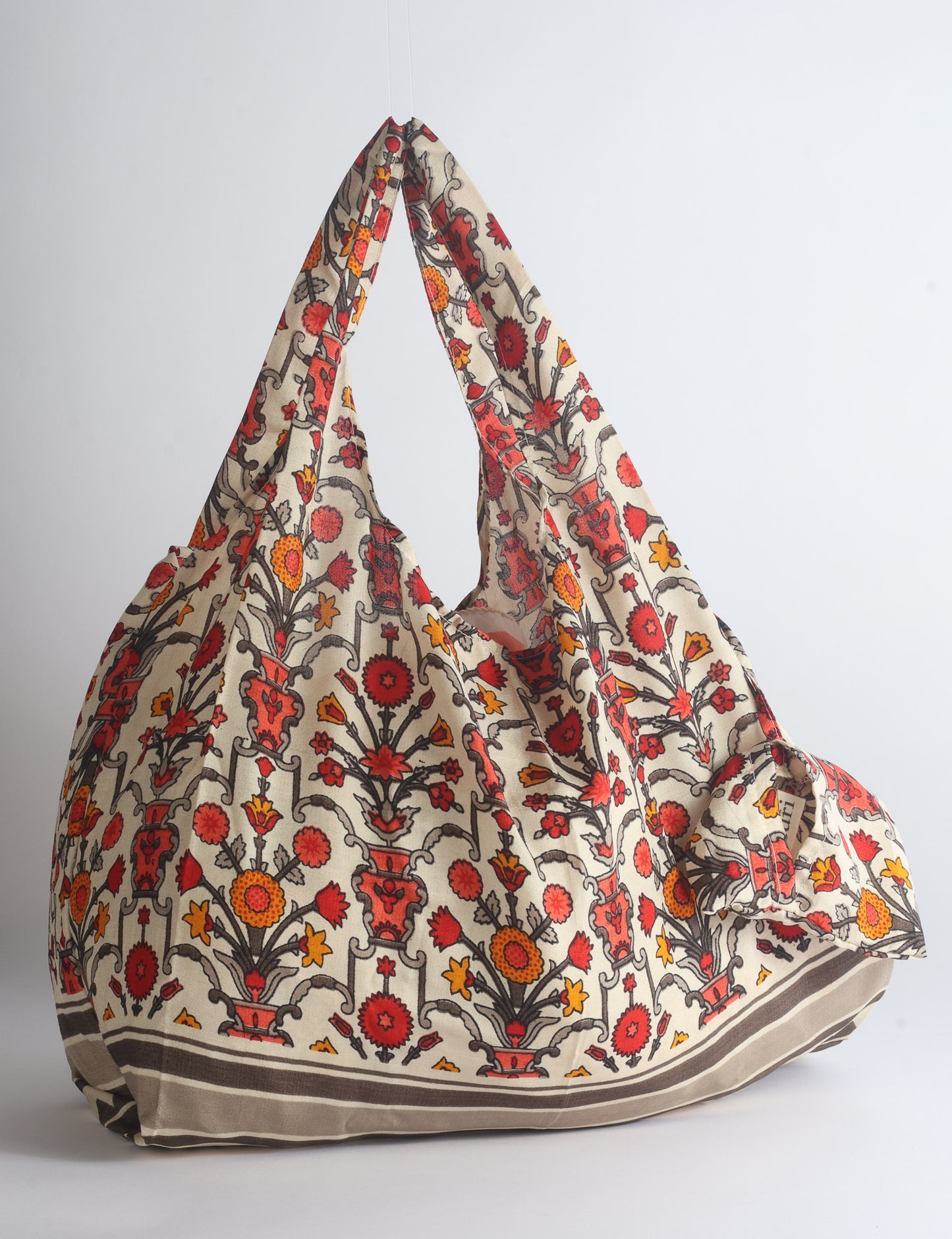 Blue reusable bag with tropical floral pattern in pink, yellow, and green, shown hanging with handles visible