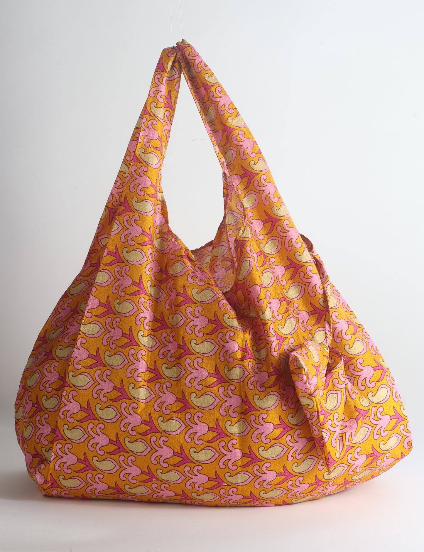 Blue reusable bag with tropical floral pattern in pink, yellow, and green, shown hanging with handles visible