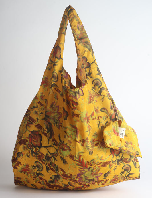 Blue reusable bag with tropical floral pattern in pink, yellow, and green, shown hanging with handles visible