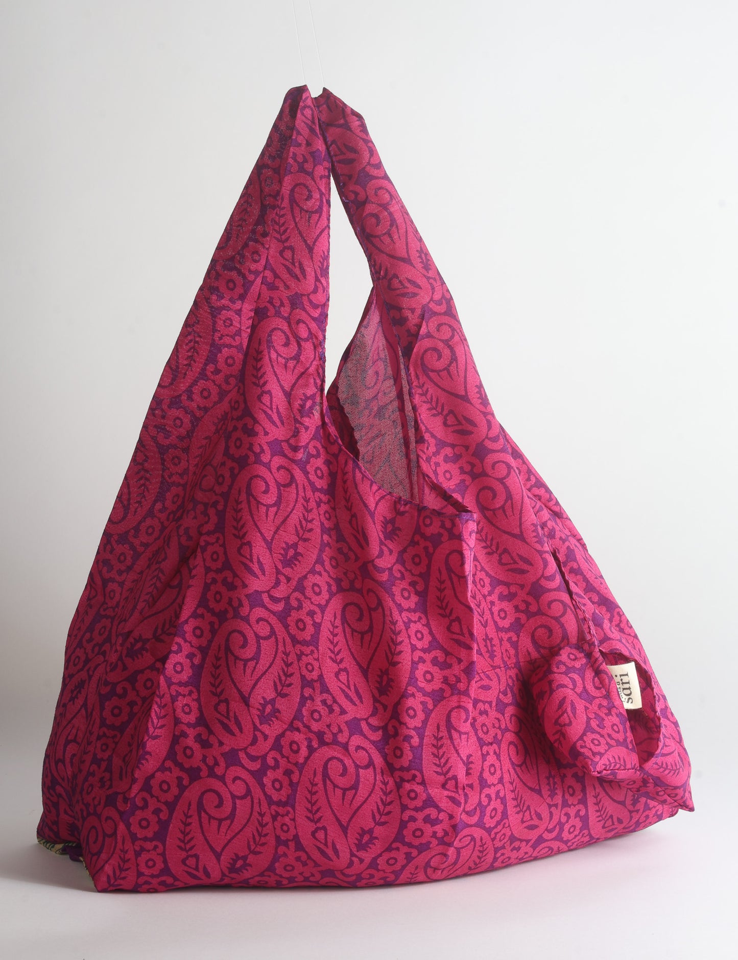 Blue reusable bag with tropical floral pattern in pink, yellow, and green, shown hanging with handles visible