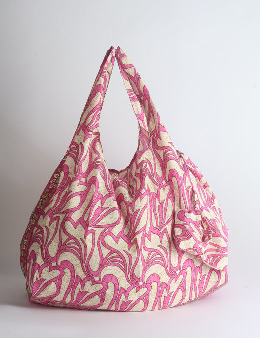 Blue reusable bag with tropical floral pattern in pink, yellow, and green, shown hanging with handles visible
