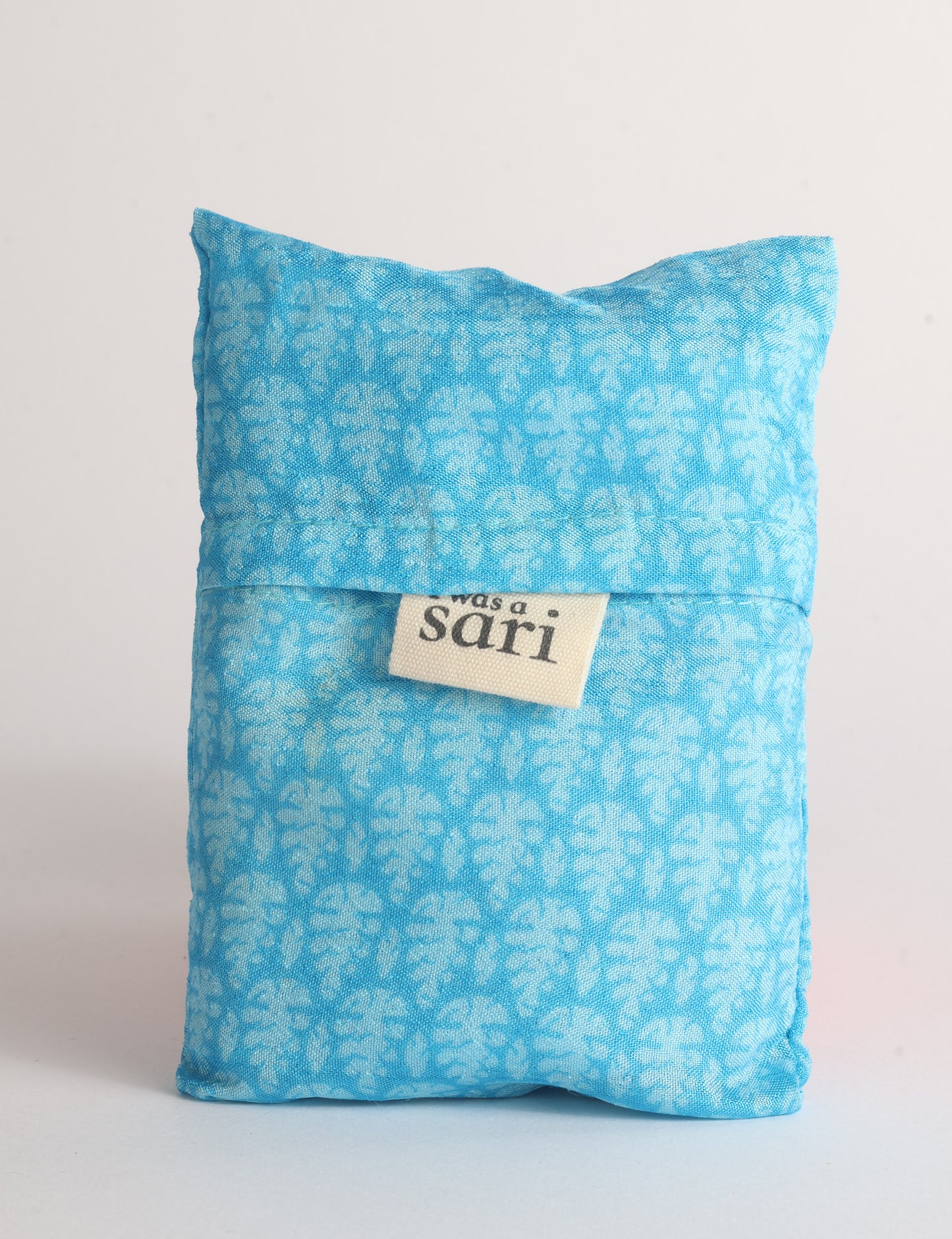 Blue reusable bag with multicolor tropical floral pattern folded with "I was a sari" label visible on front