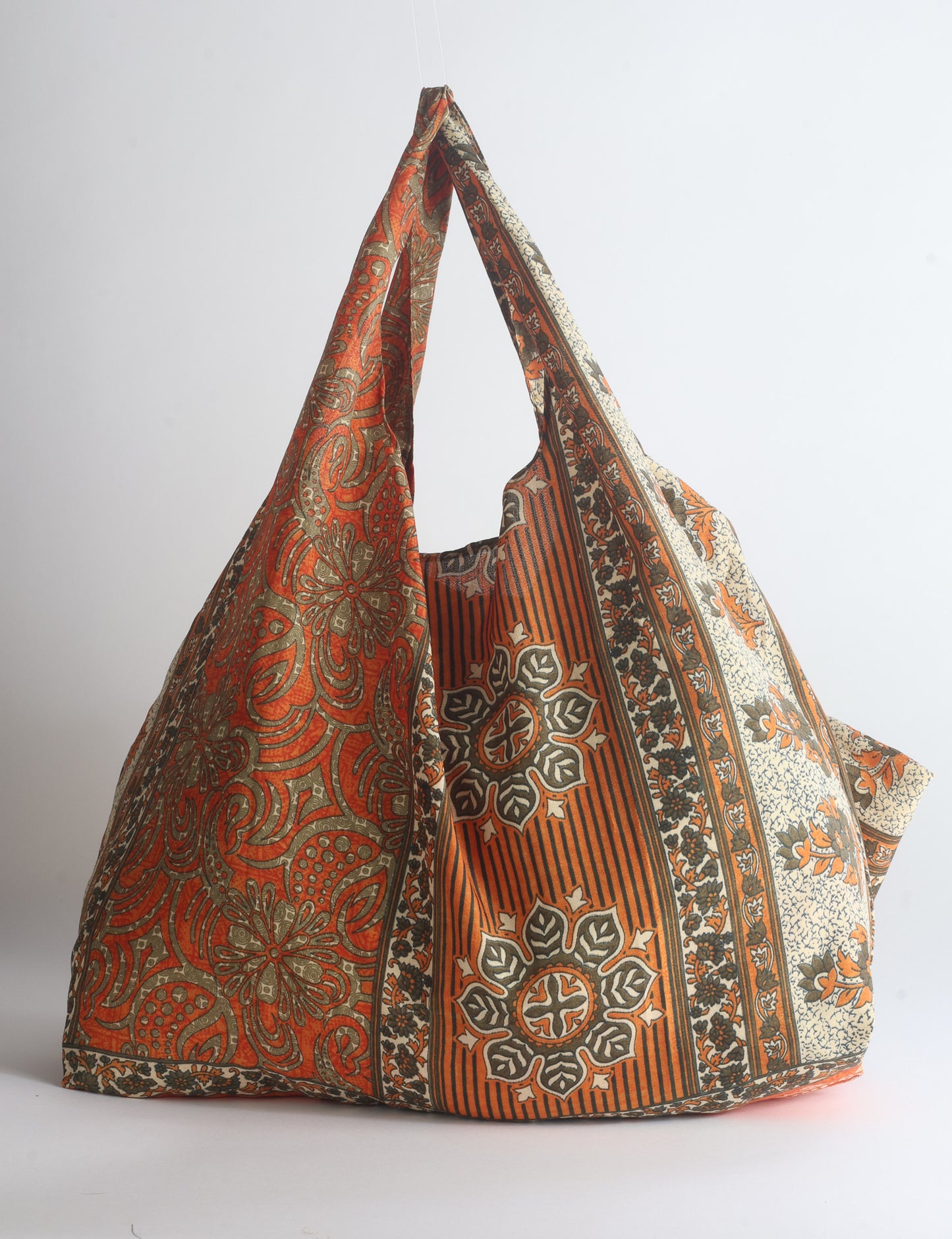 Blue reusable bag with tropical floral pattern in pink, yellow, and green, shown hanging with handles visible