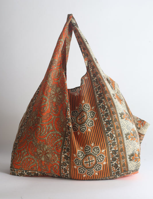 Blue reusable bag with tropical floral pattern in pink, yellow, and green, shown hanging with handles visible
