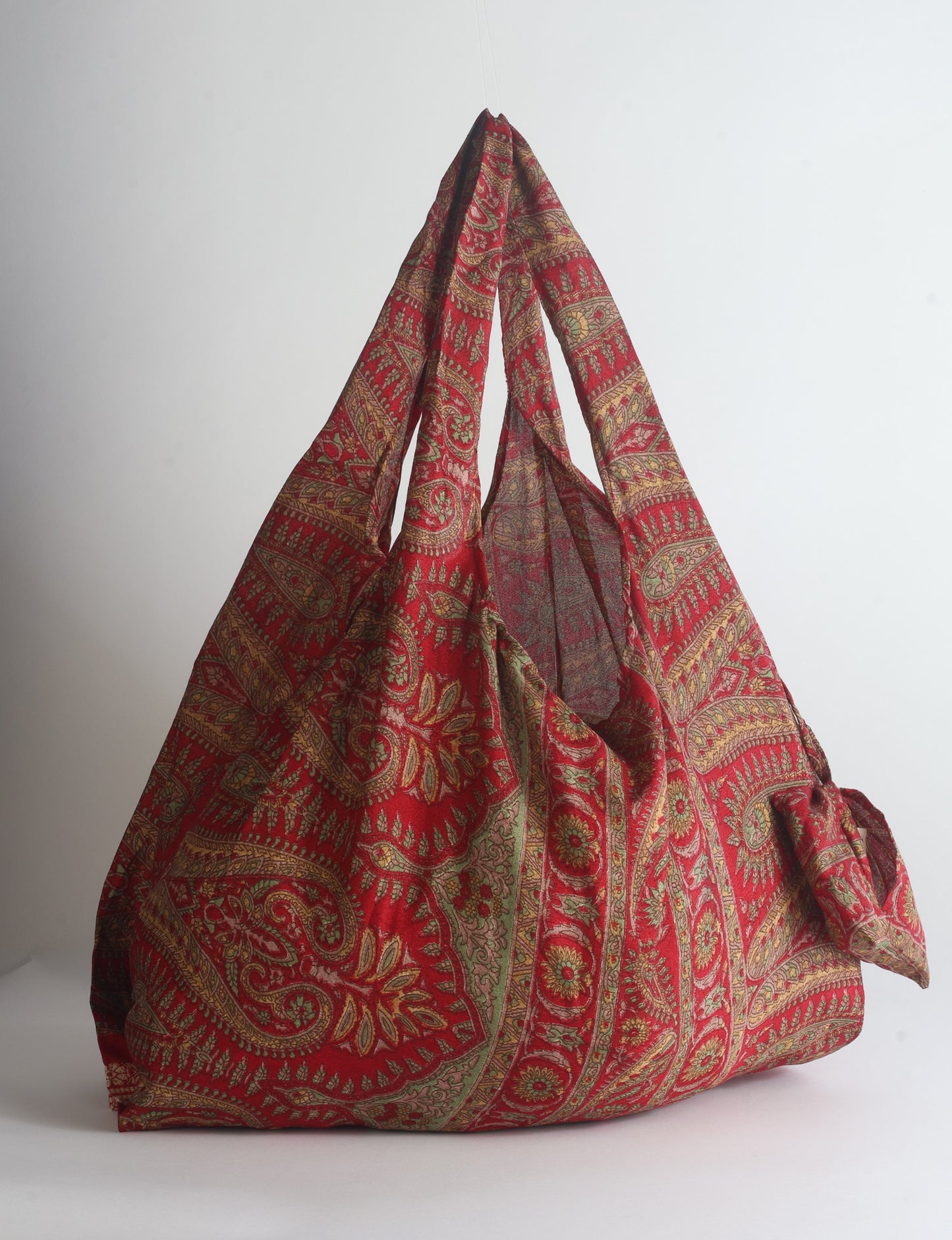 Blue reusable bag with tropical floral pattern in pink, yellow, and green, shown hanging with handles visible