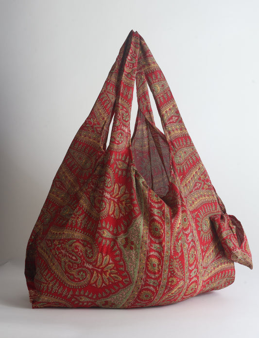 Blue reusable bag with tropical floral pattern in pink, yellow, and green, shown hanging with handles visible
