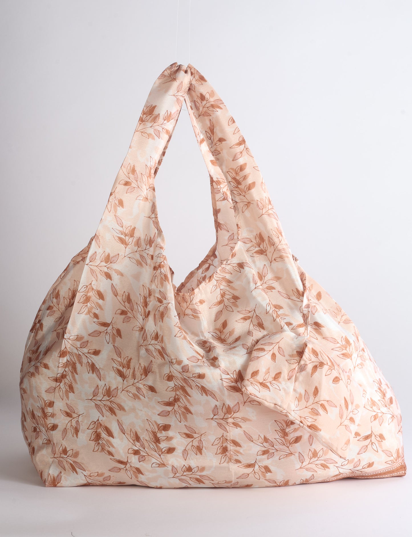 Blue reusable bag with tropical floral pattern in pink, yellow, and green, shown hanging with handles visible