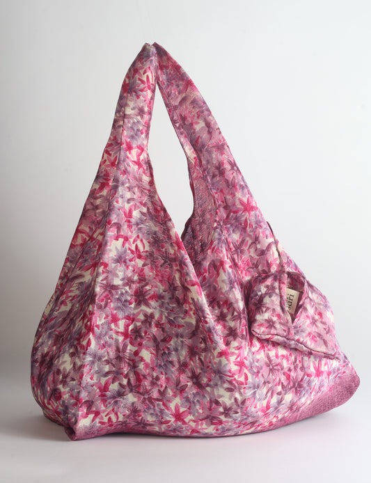 Blue reusable bag with tropical floral pattern in pink, yellow, and green, shown hanging with handles visible