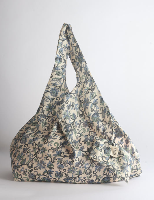 Blue reusable bag with tropical floral pattern in pink, yellow, and green, shown hanging with handles visible