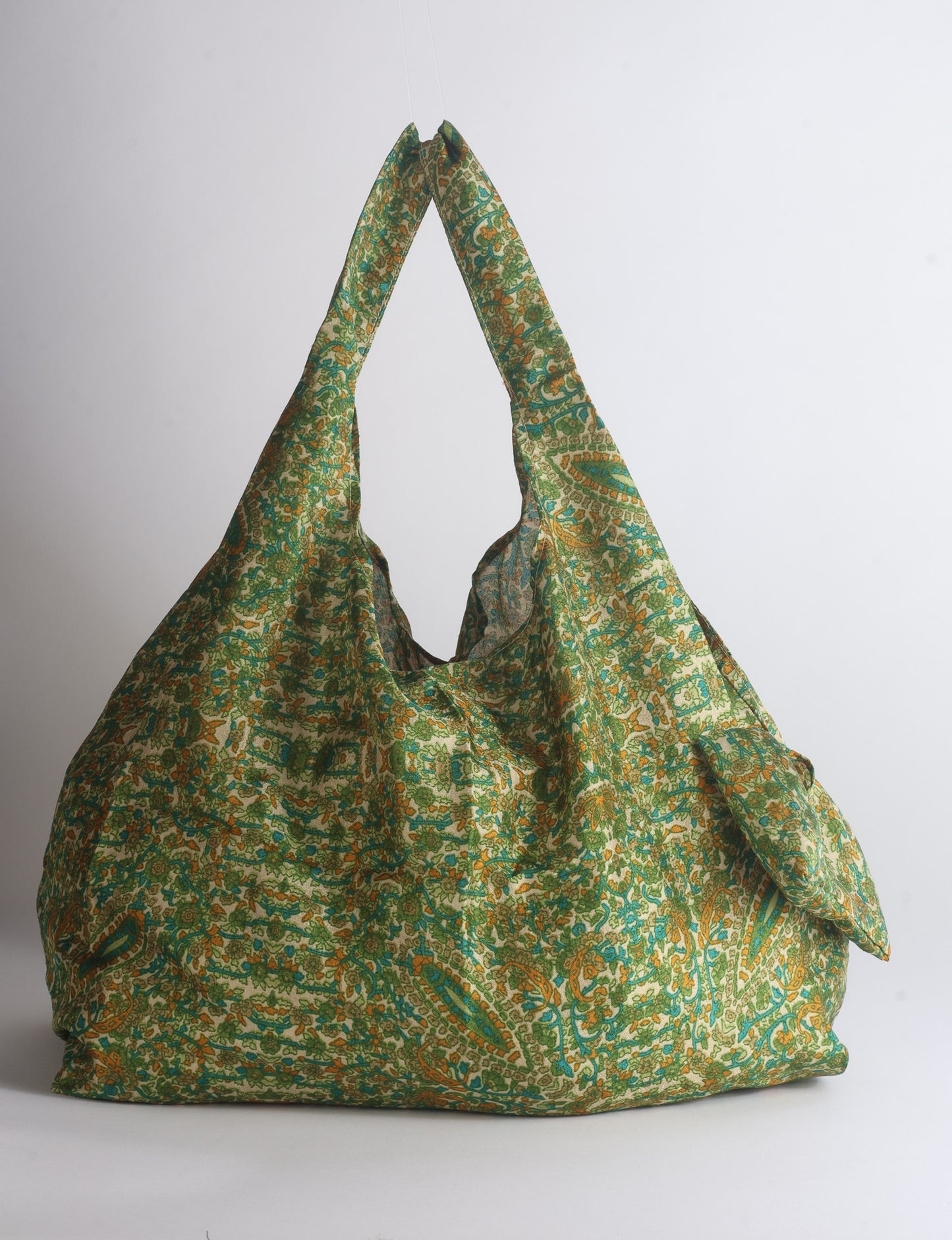 Blue reusable bag with tropical floral pattern in pink, yellow, and green, shown hanging with handles visible