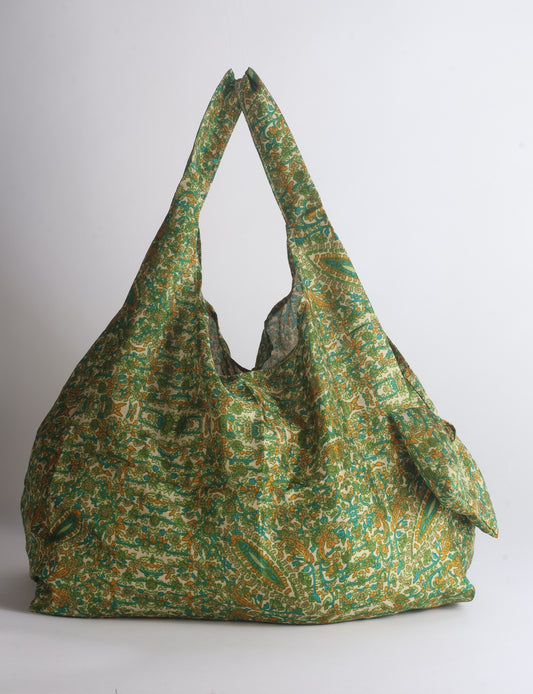 Blue reusable bag with tropical floral pattern in pink, yellow, and green, shown hanging with handles visible