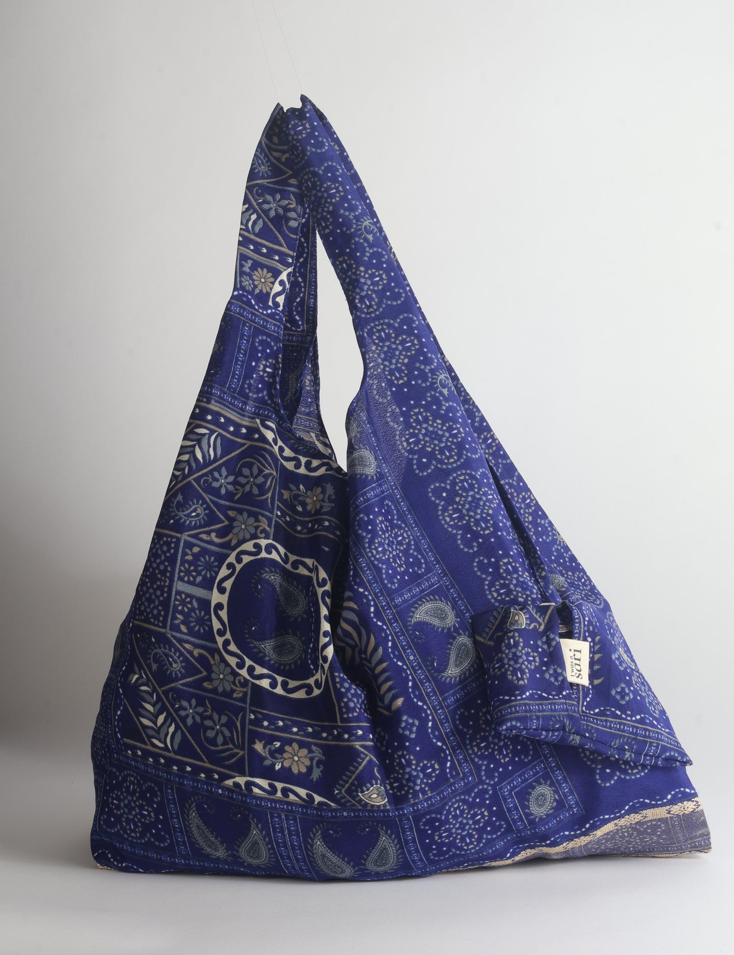 Blue reusable bag with tropical floral pattern in pink, yellow, and green, shown hanging with handles visible