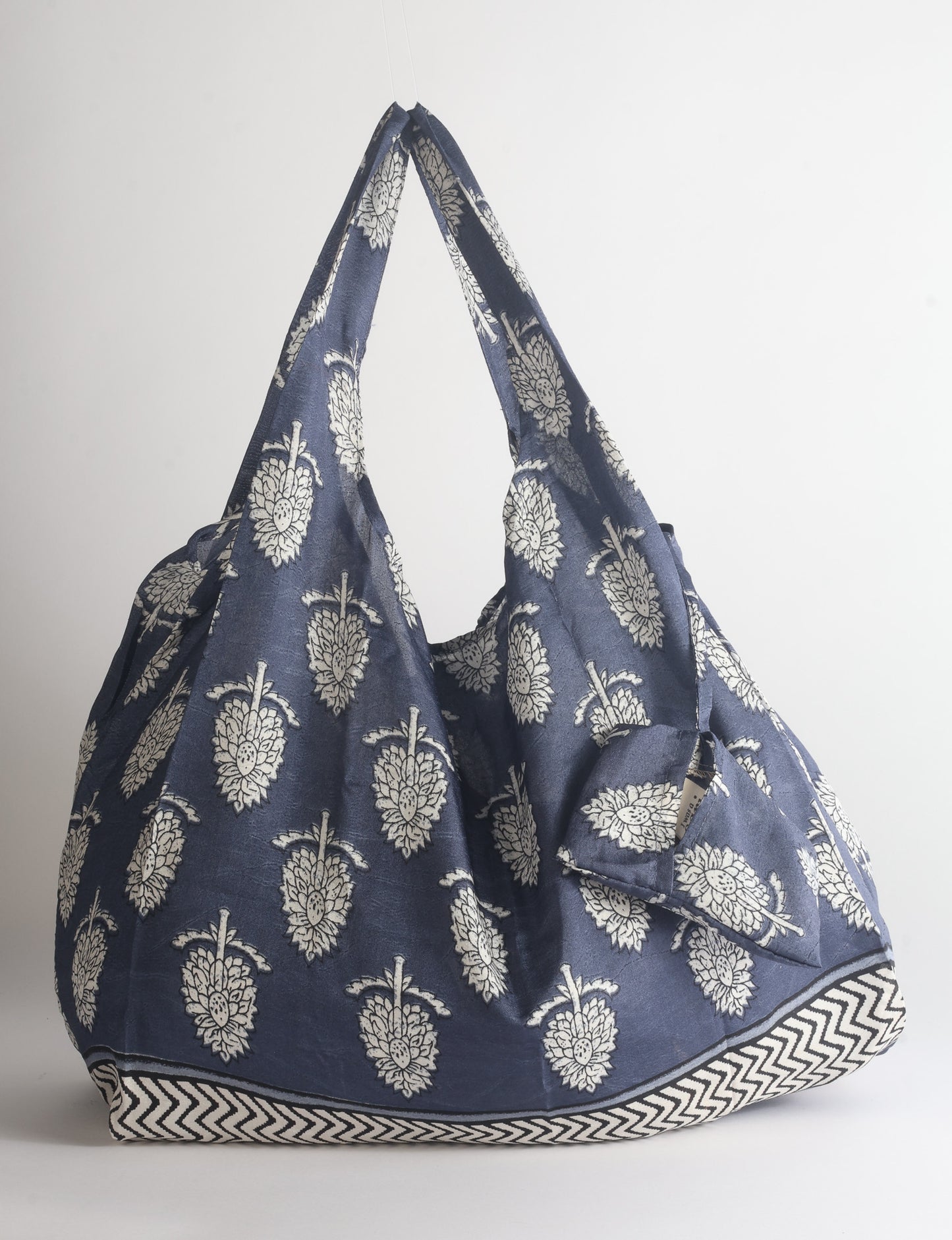 Blue reusable bag with tropical floral pattern in pink, yellow, and green, shown hanging with handles visible