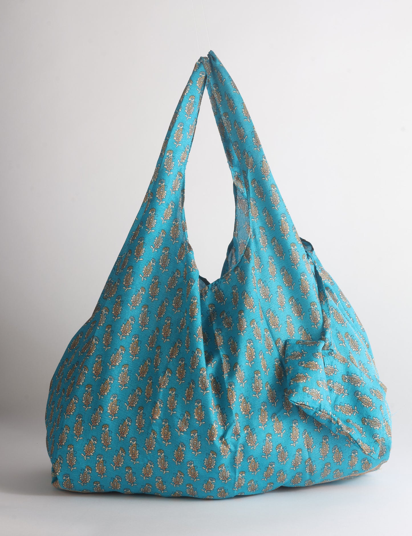 Blue reusable bag with tropical floral pattern in pink, yellow, and green, shown hanging with handles visible
