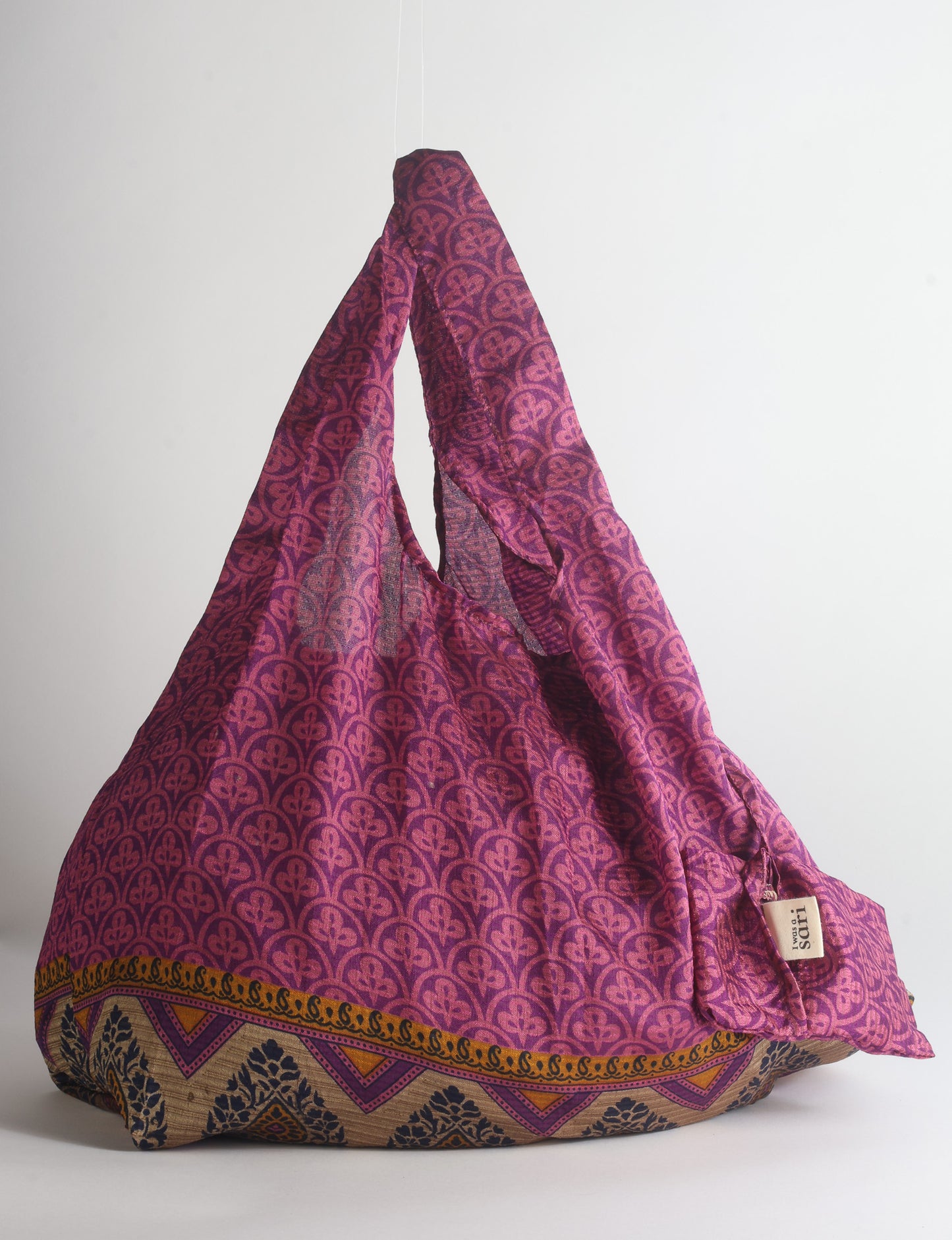 Blue reusable bag with tropical floral pattern in pink, yellow, and green, shown hanging with handles visible