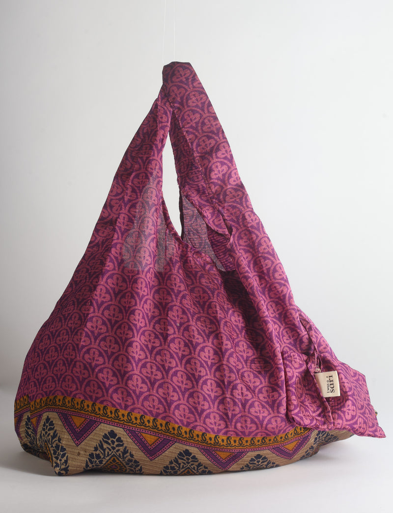 Blue reusable bag with tropical floral pattern in pink, yellow, and green, shown hanging with handles visible