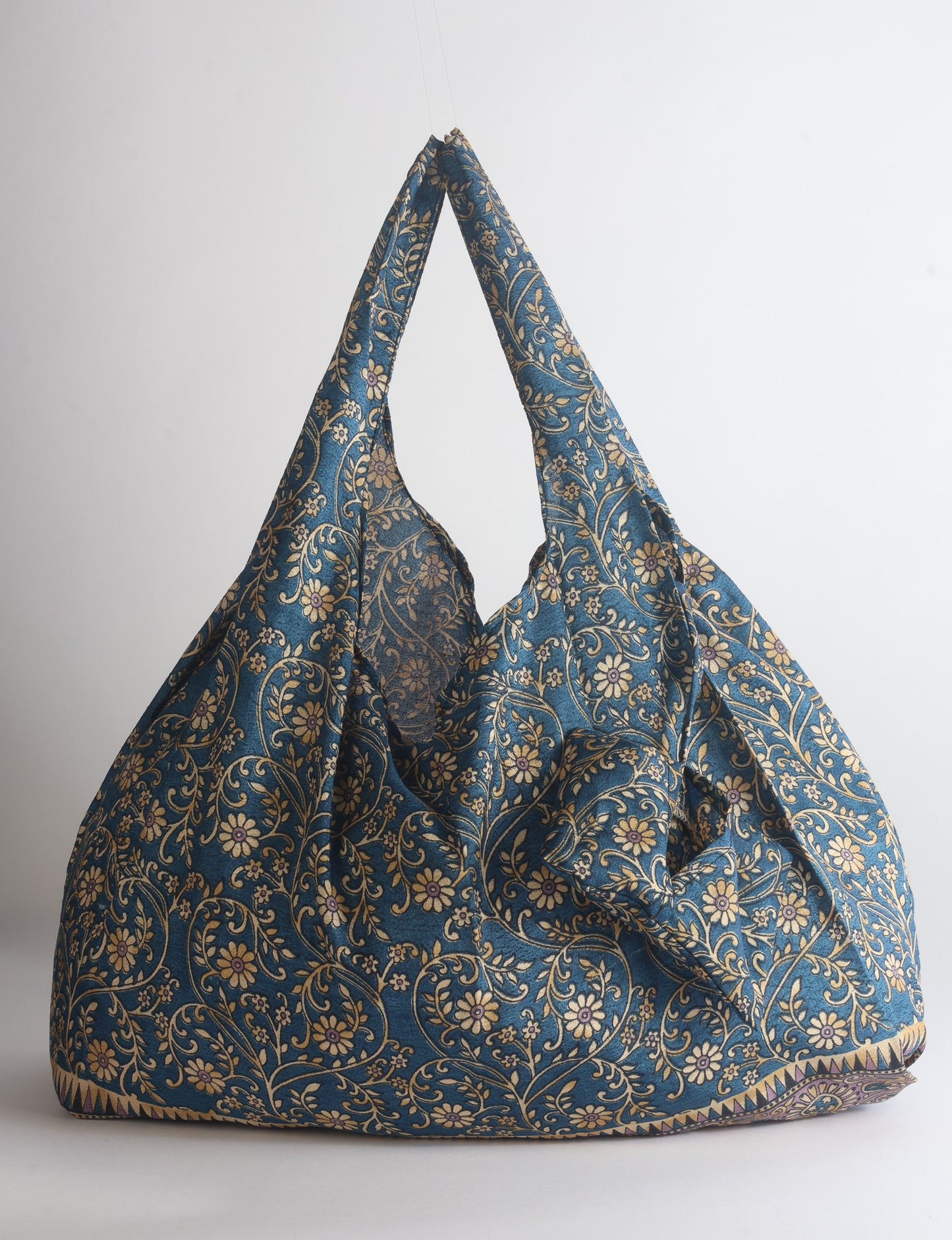 Blue reusable bag with tropical floral pattern in pink, yellow, and green, shown hanging with handles visible