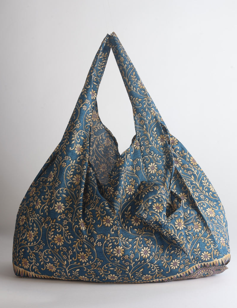Blue reusable bag with tropical floral pattern in pink, yellow, and green, shown hanging with handles visible