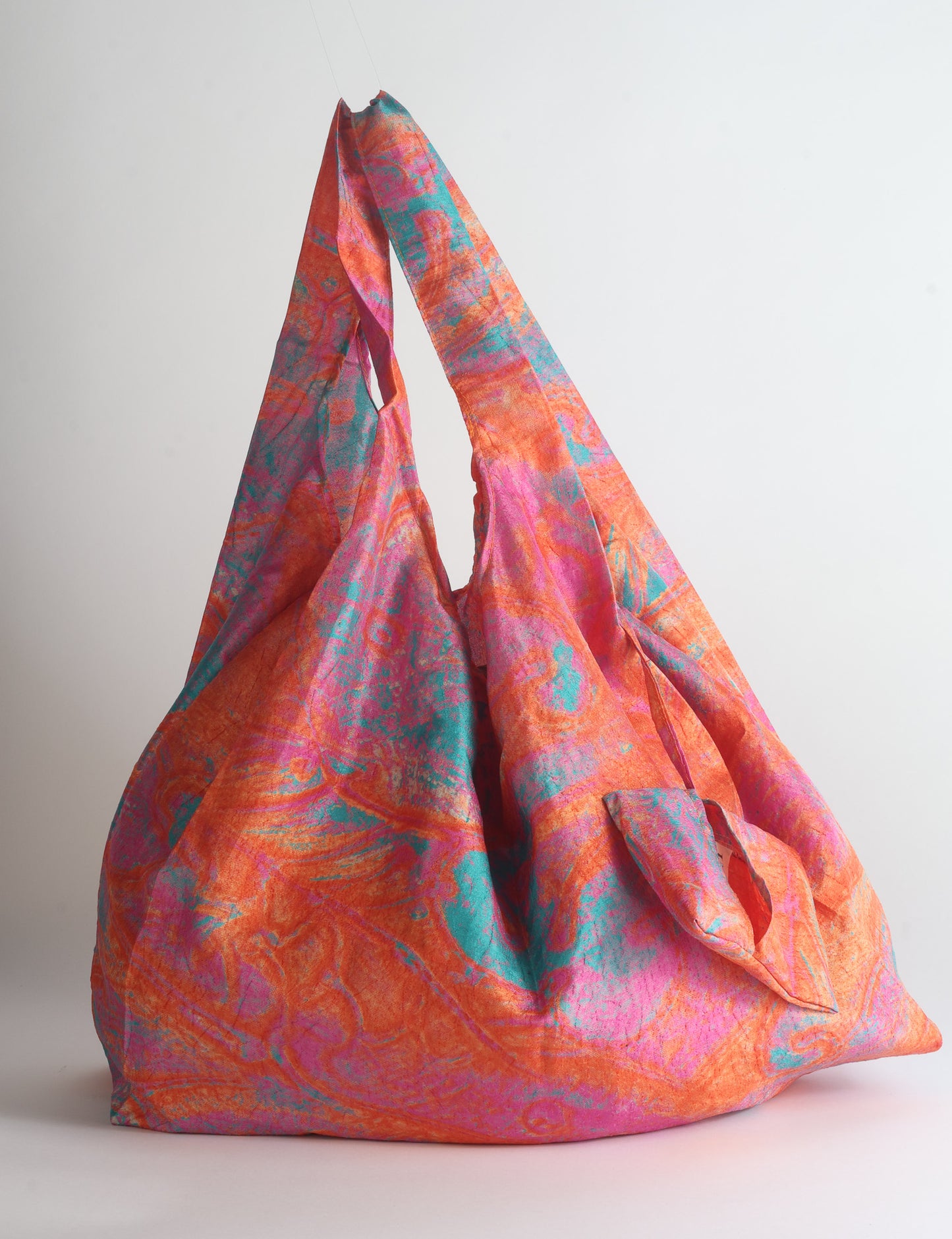 Blue reusable bag with tropical floral pattern in pink, yellow, and green, shown hanging with handles visible