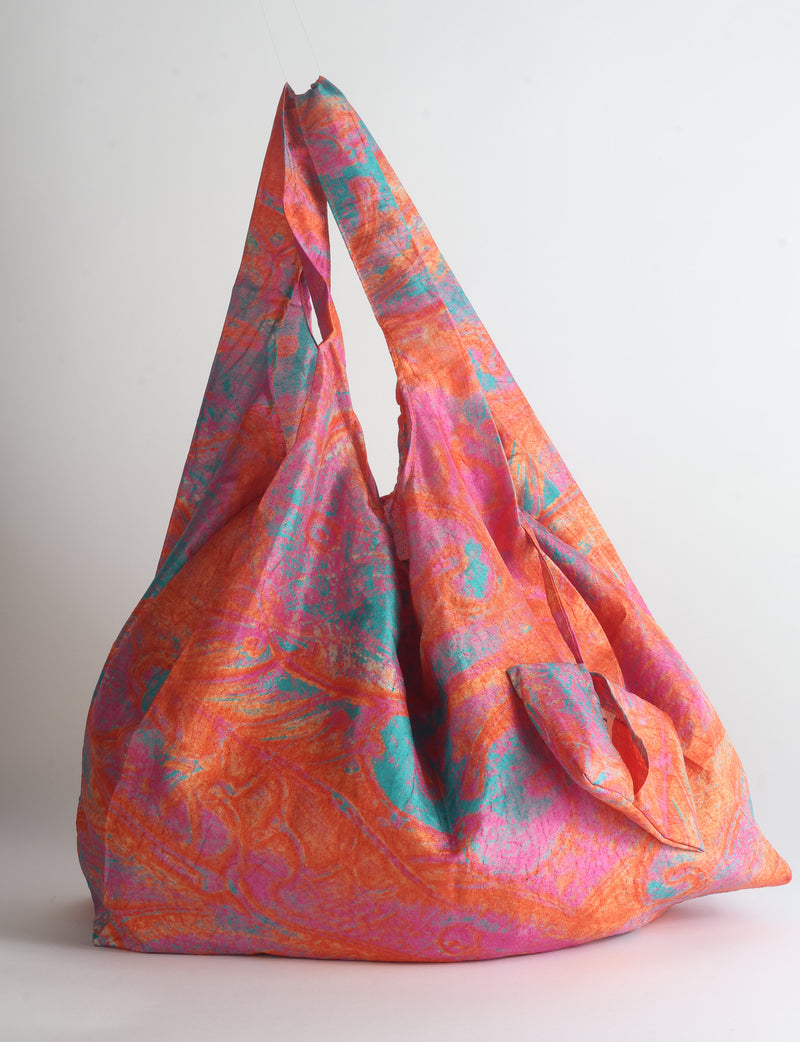 Blue reusable bag with tropical floral pattern in pink, yellow, and green, shown hanging with handles visible