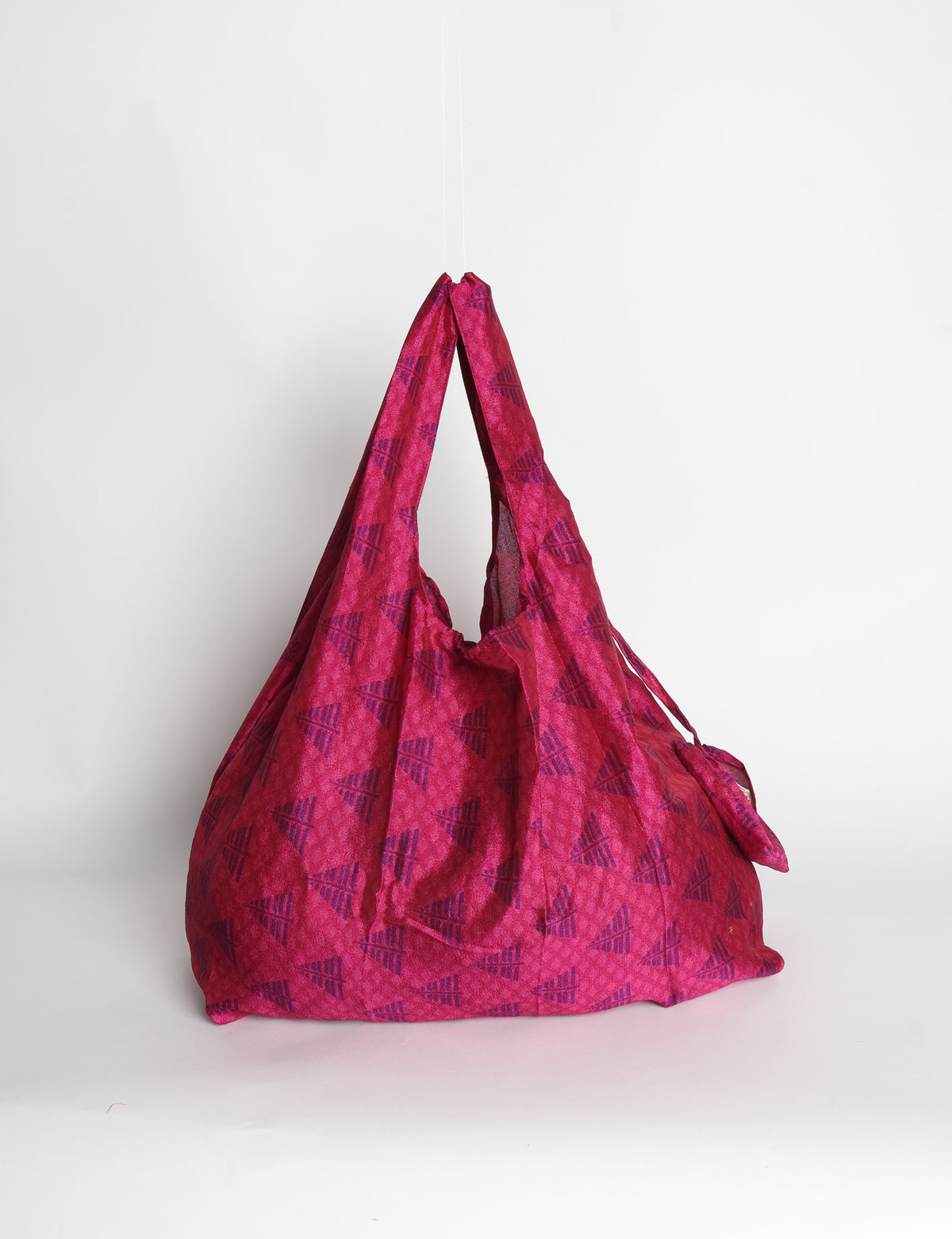 Blue reusable bag with tropical floral pattern in pink, yellow, and green, shown hanging with handles visible