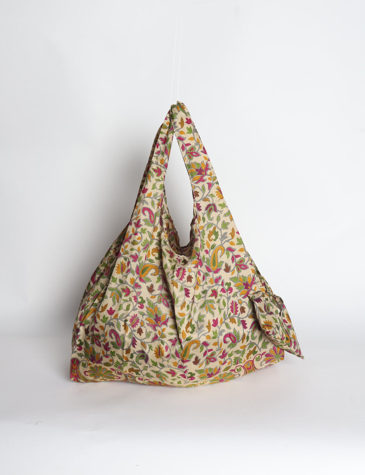 Blue reusable bag with tropical floral pattern in pink, yellow, and green, shown hanging with handles visible