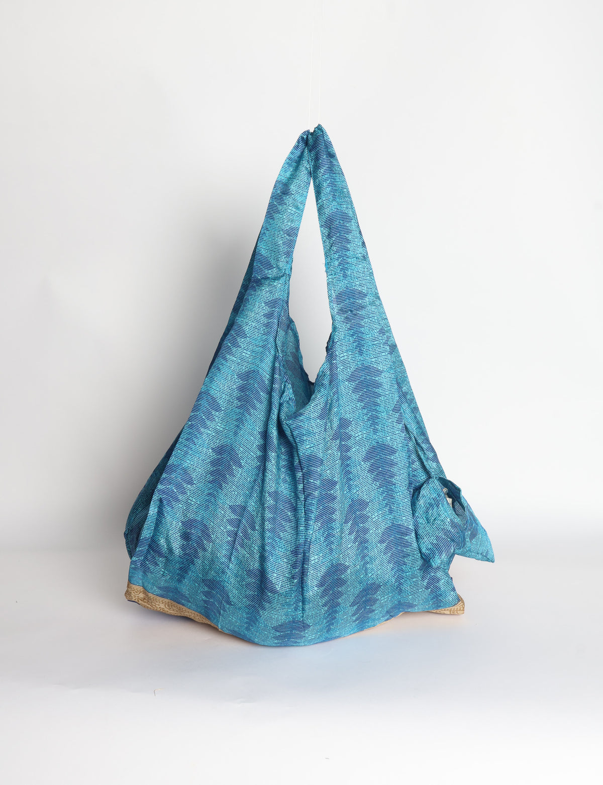 Blue reusable bag with tropical floral pattern in pink, yellow, and green, shown hanging with handles visible