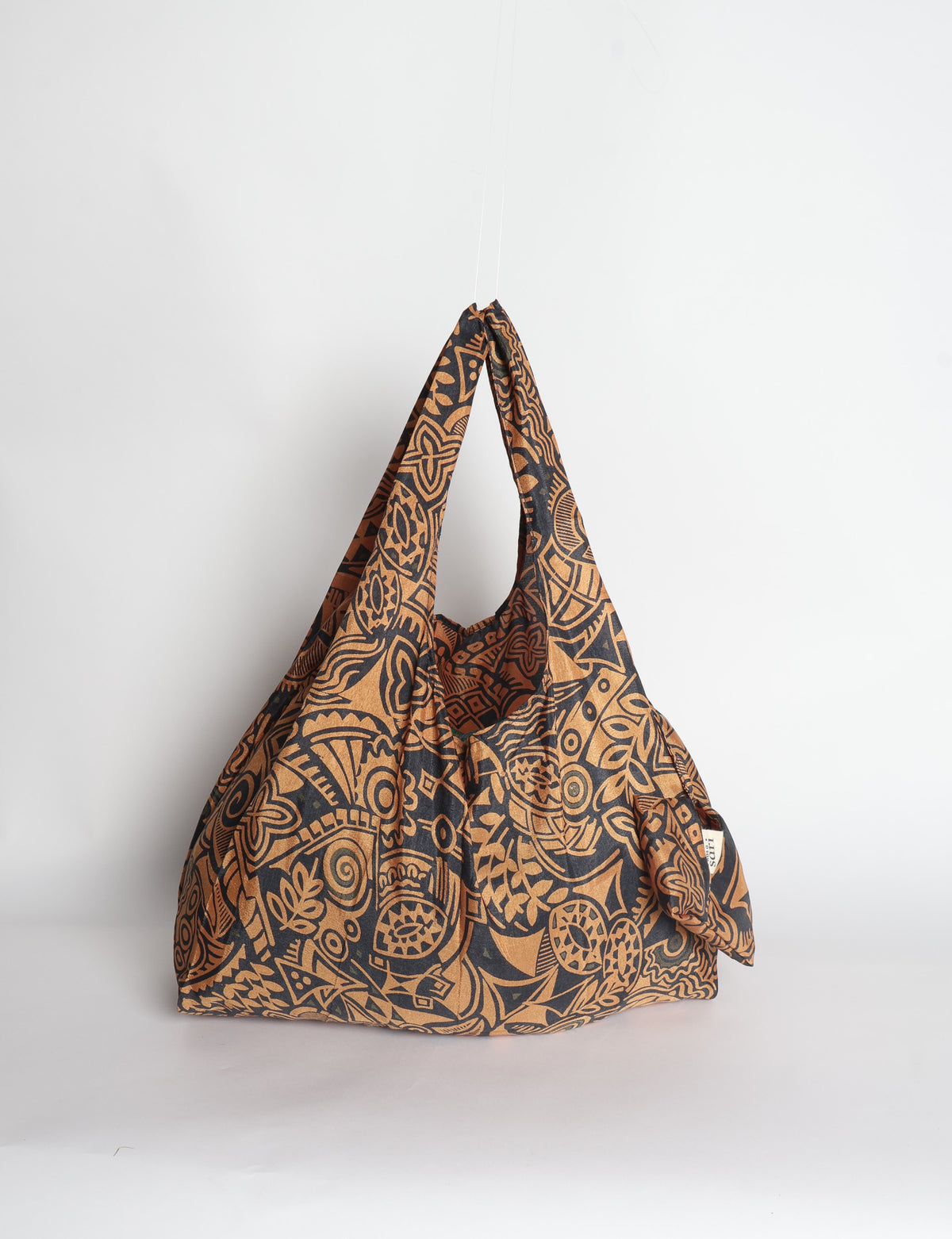 Blue reusable bag with tropical floral pattern in pink, yellow, and green, shown hanging with handles visible