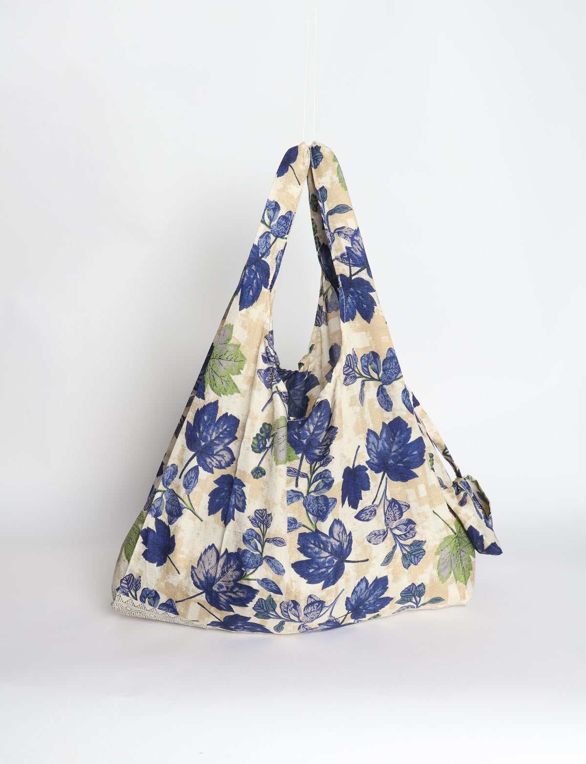 Blue reusable bag with tropical floral pattern in pink, yellow, and green, shown hanging with handles visible