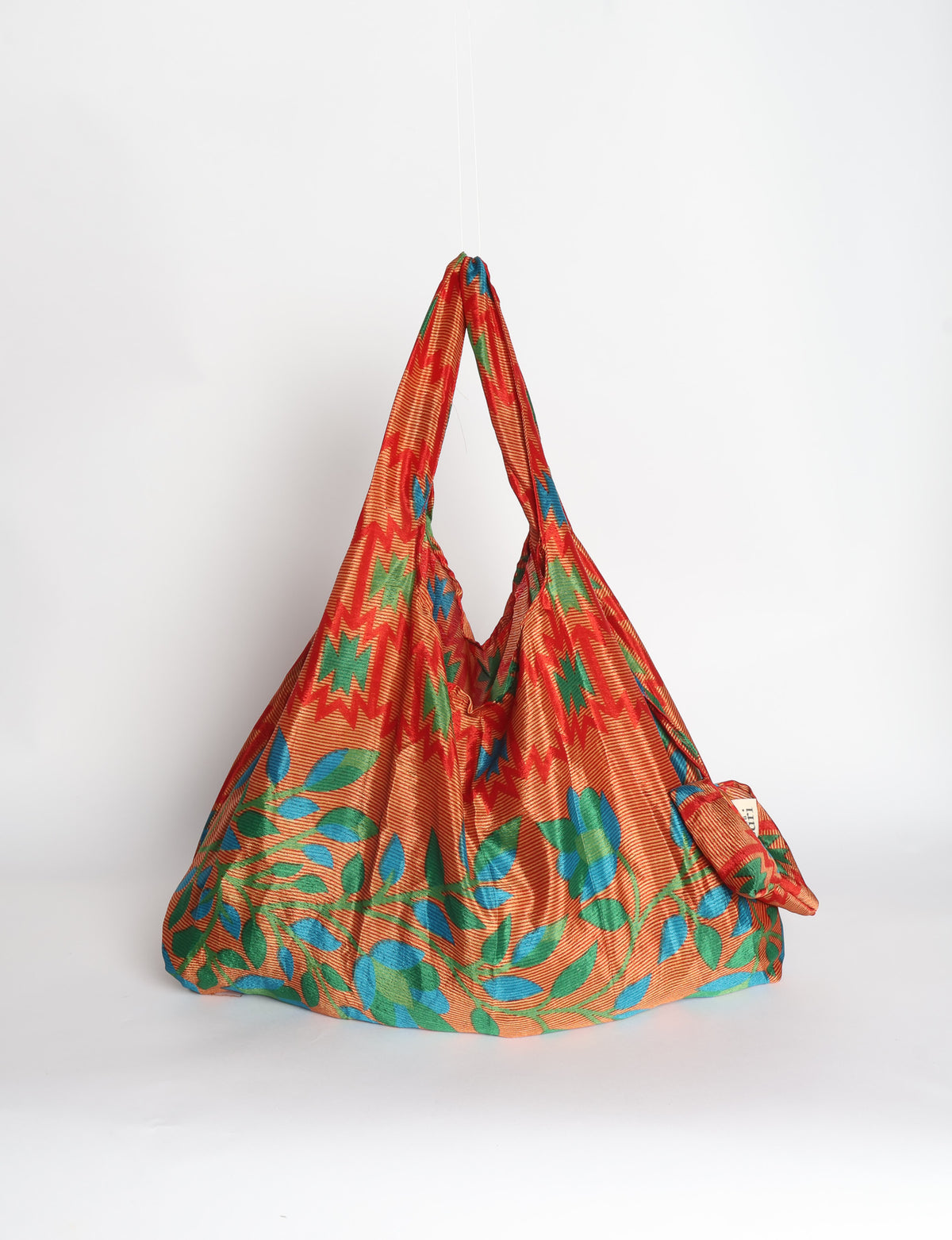 Blue reusable bag with tropical floral pattern in pink, yellow, and green, shown hanging with handles visible