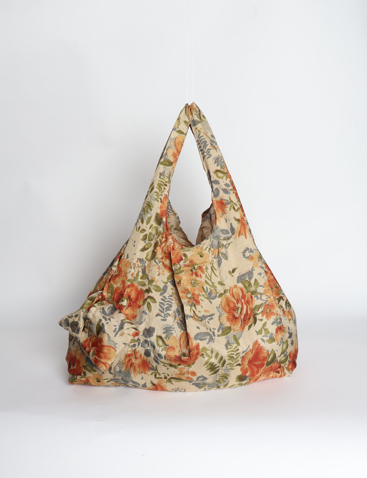 Blue reusable bag with tropical floral pattern in pink, yellow, and green, shown hanging with handles visible
