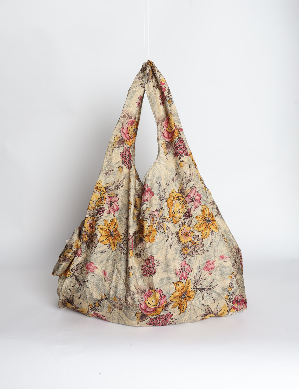 Blue reusable bag with tropical floral pattern in pink, yellow, and green, shown hanging with handles visible