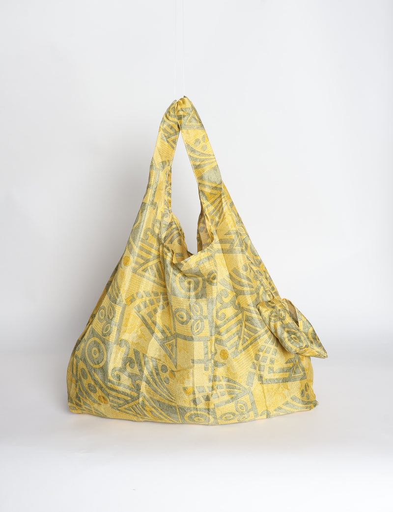 Blue reusable bag with tropical floral pattern in pink, yellow, and green, shown hanging with handles visible