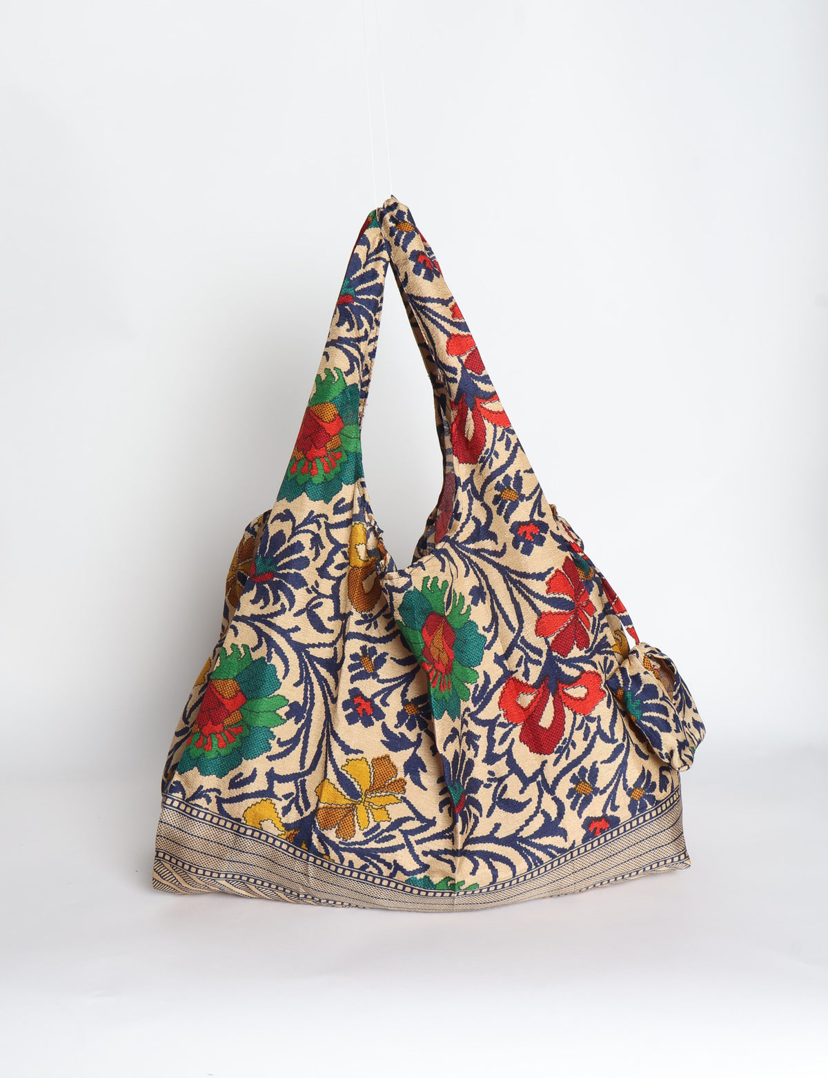 Blue reusable bag with tropical floral pattern in pink, yellow, and green, shown hanging with handles visible