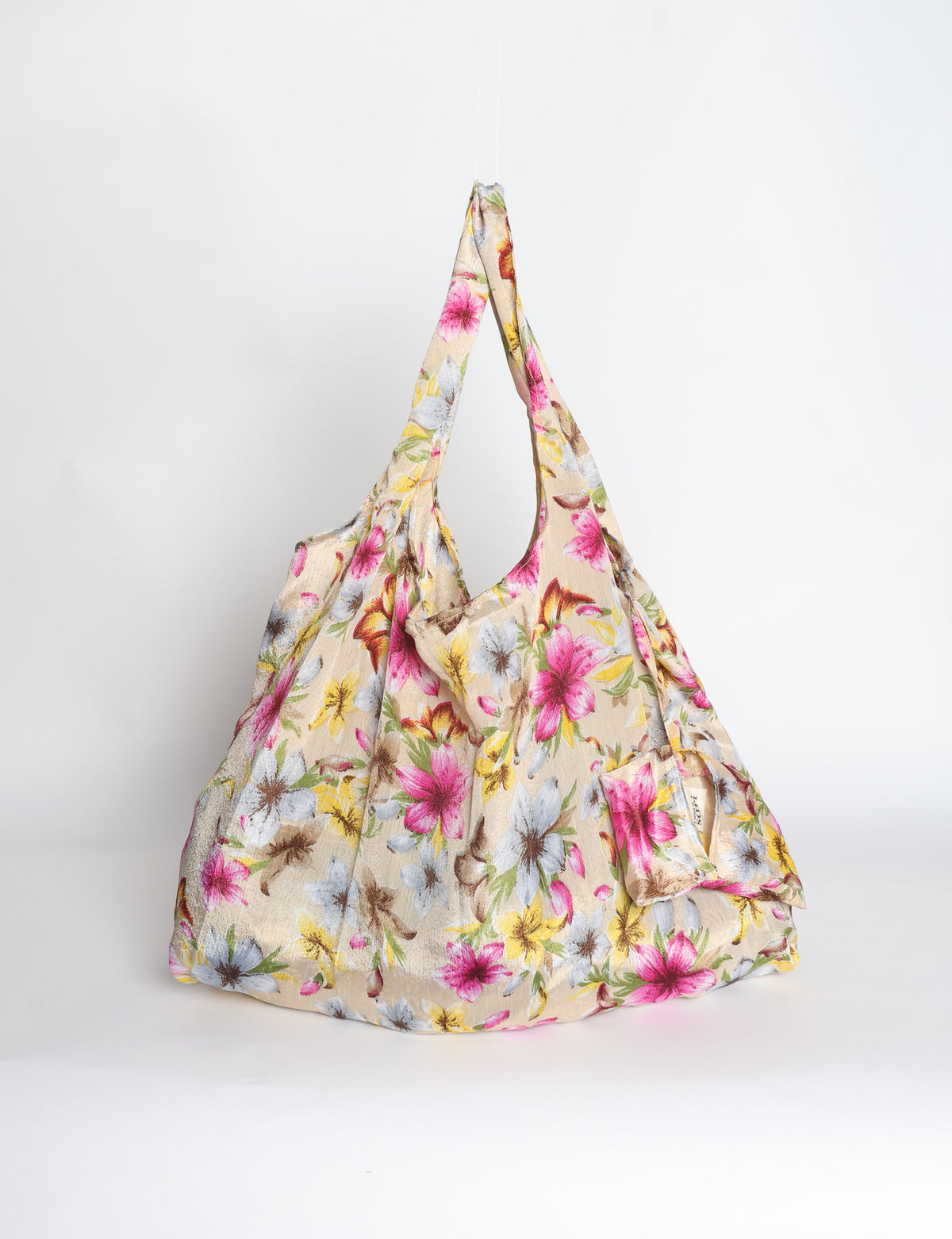 Blue reusable bag with tropical floral pattern in pink, yellow, and green, shown hanging with handles visible