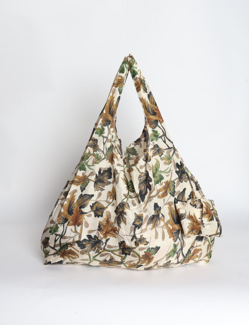 Blue reusable bag with tropical floral pattern in pink, yellow, and green, shown hanging with handles visible