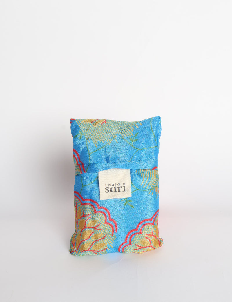 Blue reusable bag with multicolor tropical floral pattern folded with "I was a sari" label visible on front