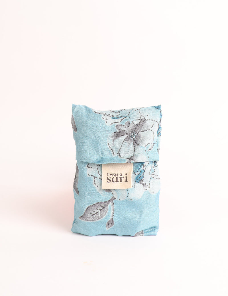 Blue reusable bag with multicolor tropical floral pattern folded with "I was a sari" label visible on front