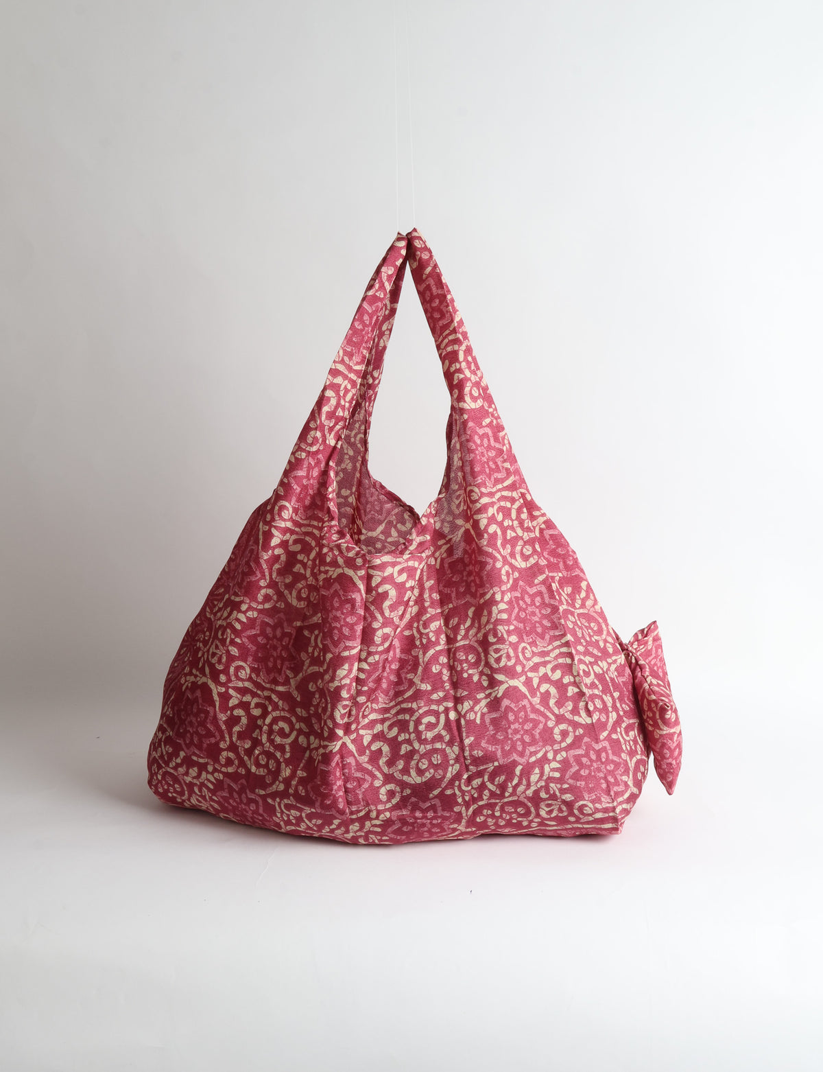 Blue reusable bag with tropical floral pattern in pink, yellow, and green, shown hanging with handles visible