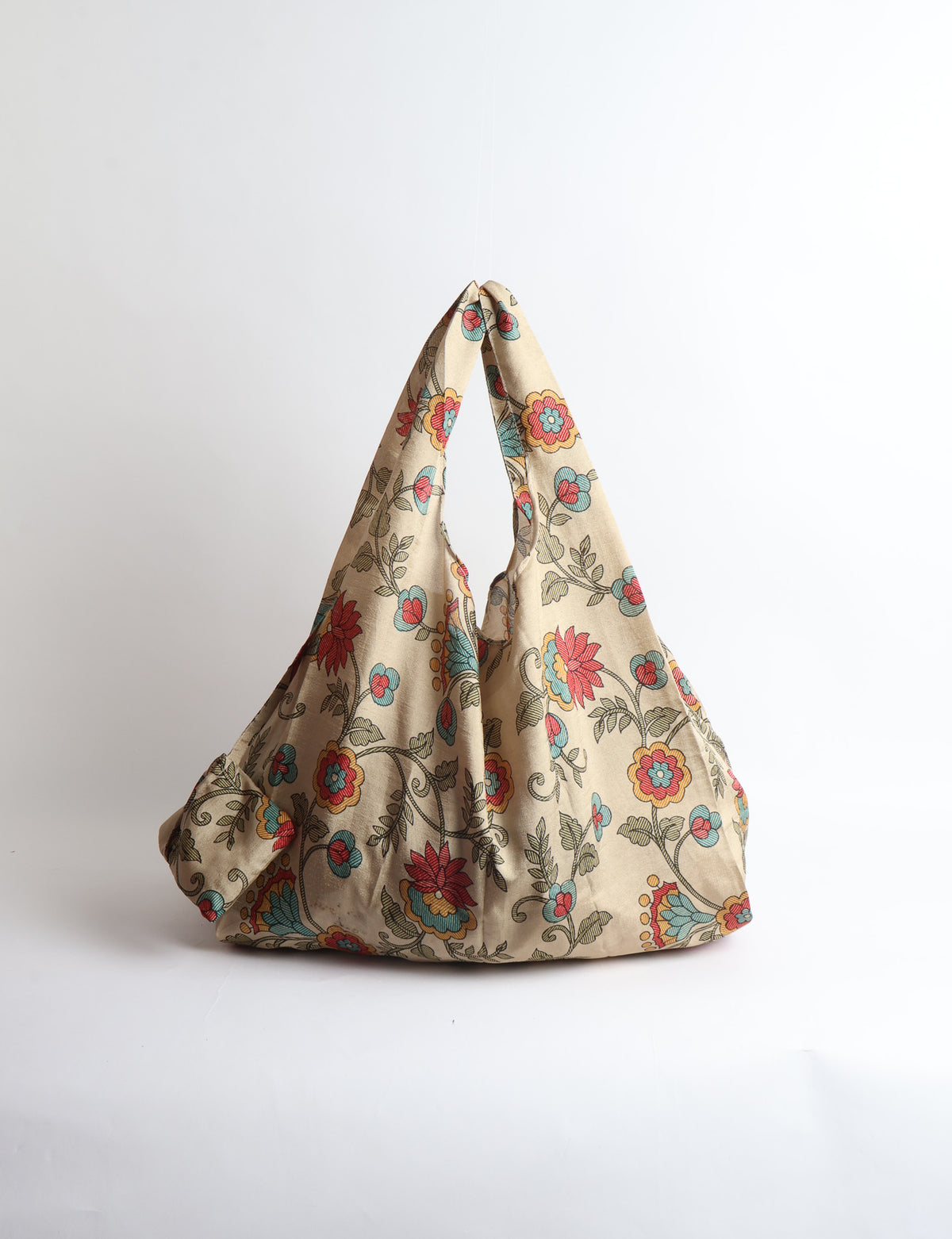 Blue reusable bag with tropical floral pattern in pink, yellow, and green, shown hanging with handles visible