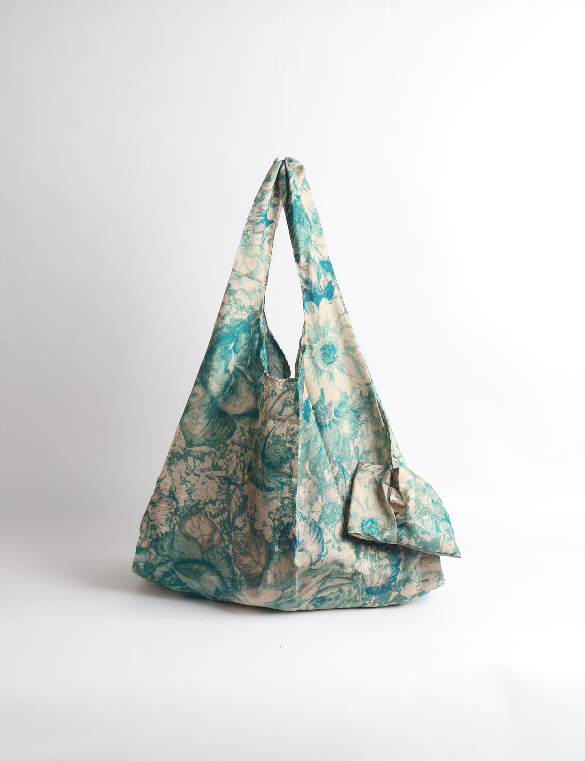 Blue reusable bag with tropical floral pattern in pink, yellow, and green, shown hanging with handles visible