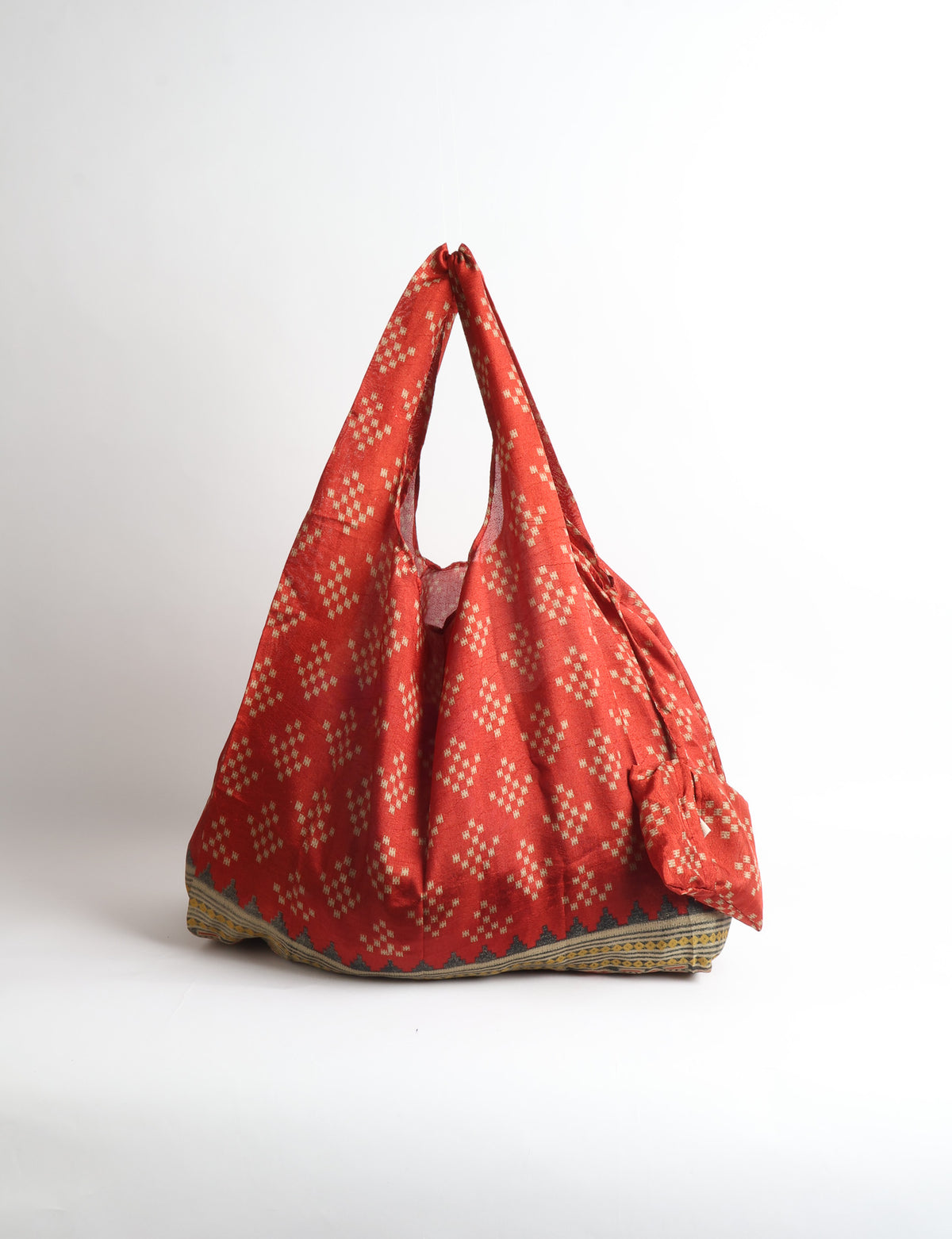 Blue reusable bag with tropical floral pattern in pink, yellow, and green, shown hanging with handles visible